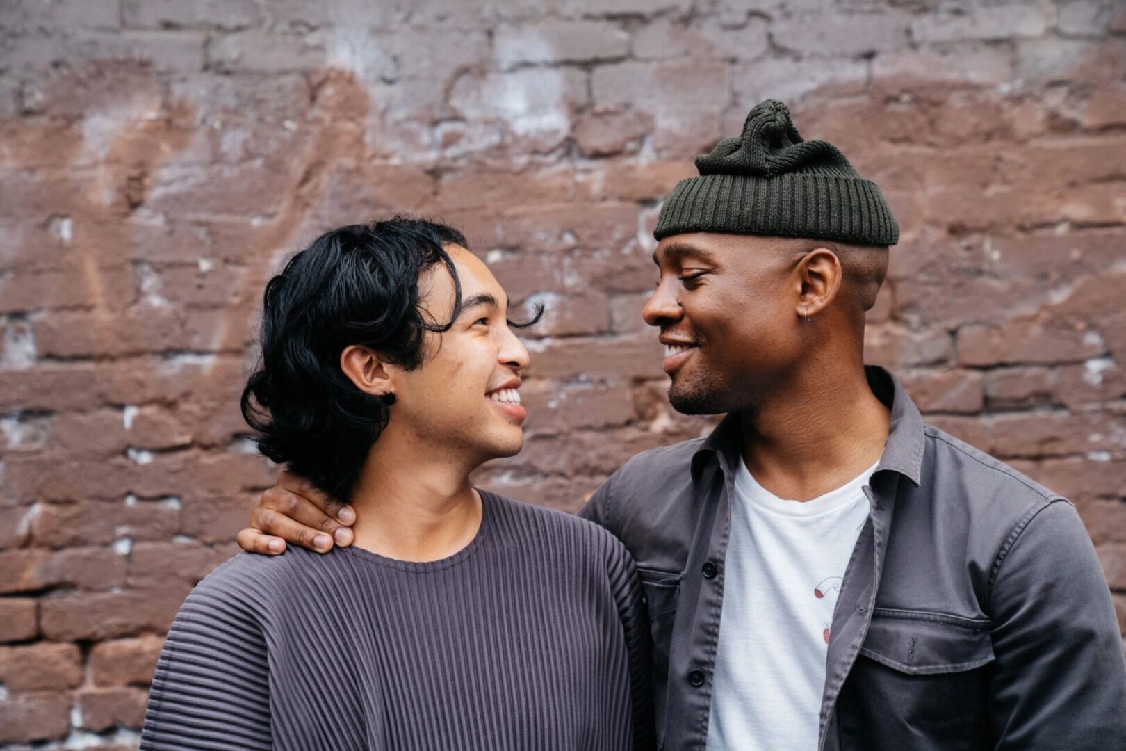 Two people standing next to each other near a brick wall.