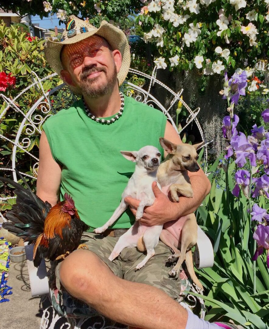 A man sitting in front of some flowers with two small animals.